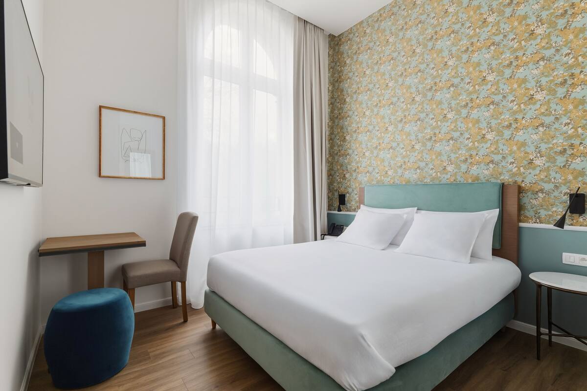 Een hotelkamer met een bed, een bureau, een stoel en een klein tafeltje.