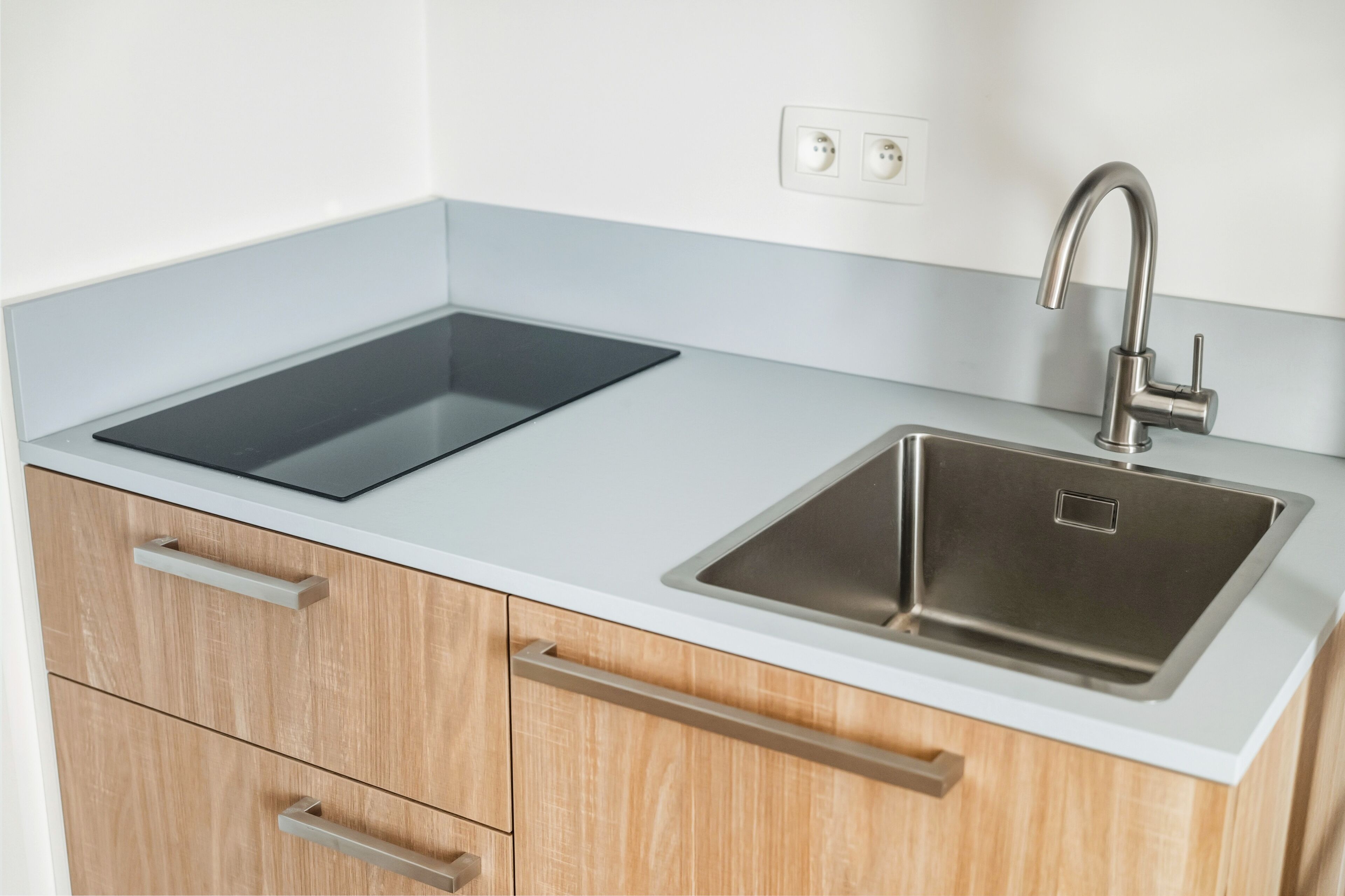 A kitchen with a stainless steel sink, a black induction cooktop, and wooden cabinets.