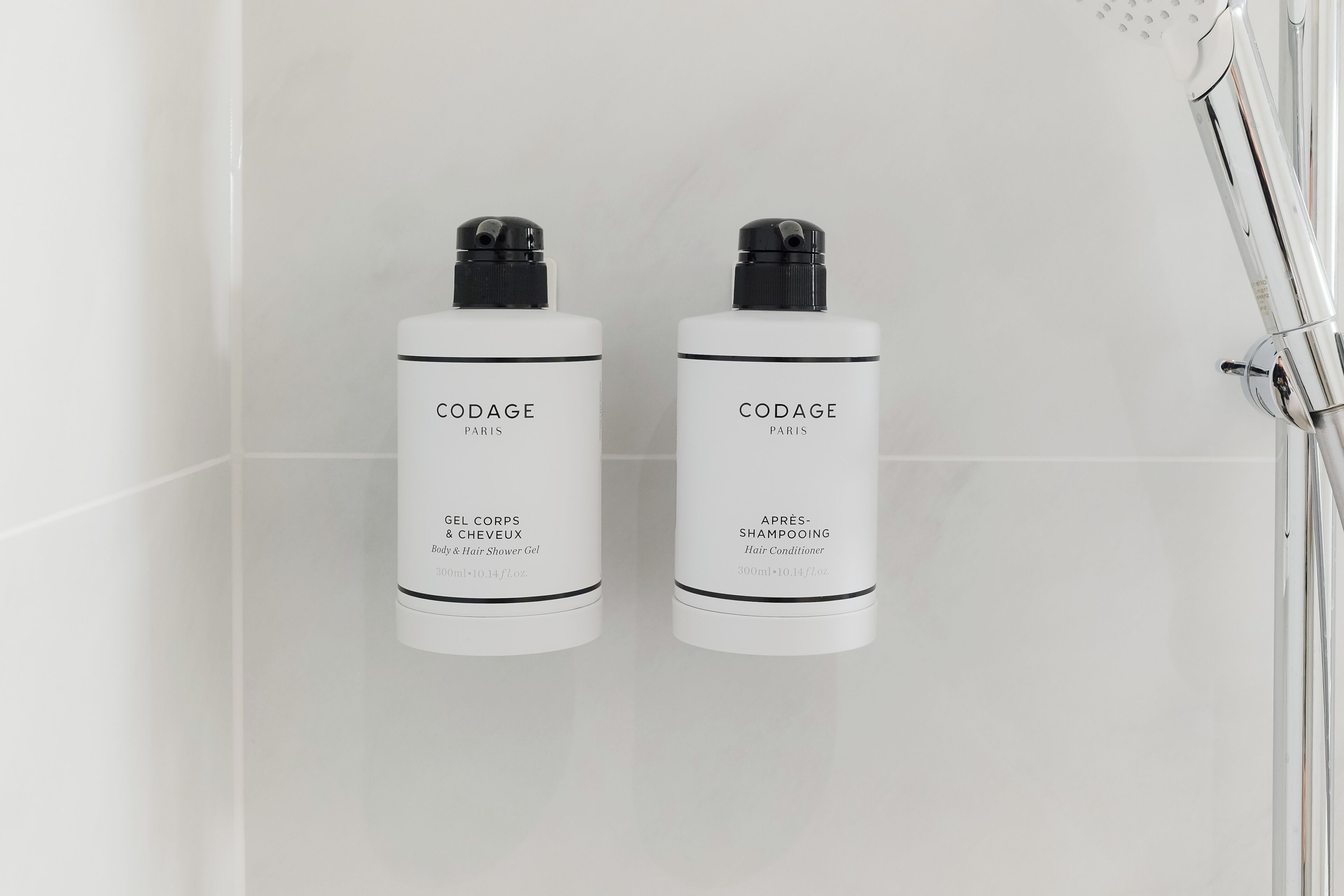 Dos botellas blancas de productos capilares CODAGE Paris sobre una pared de azulejos blancos.