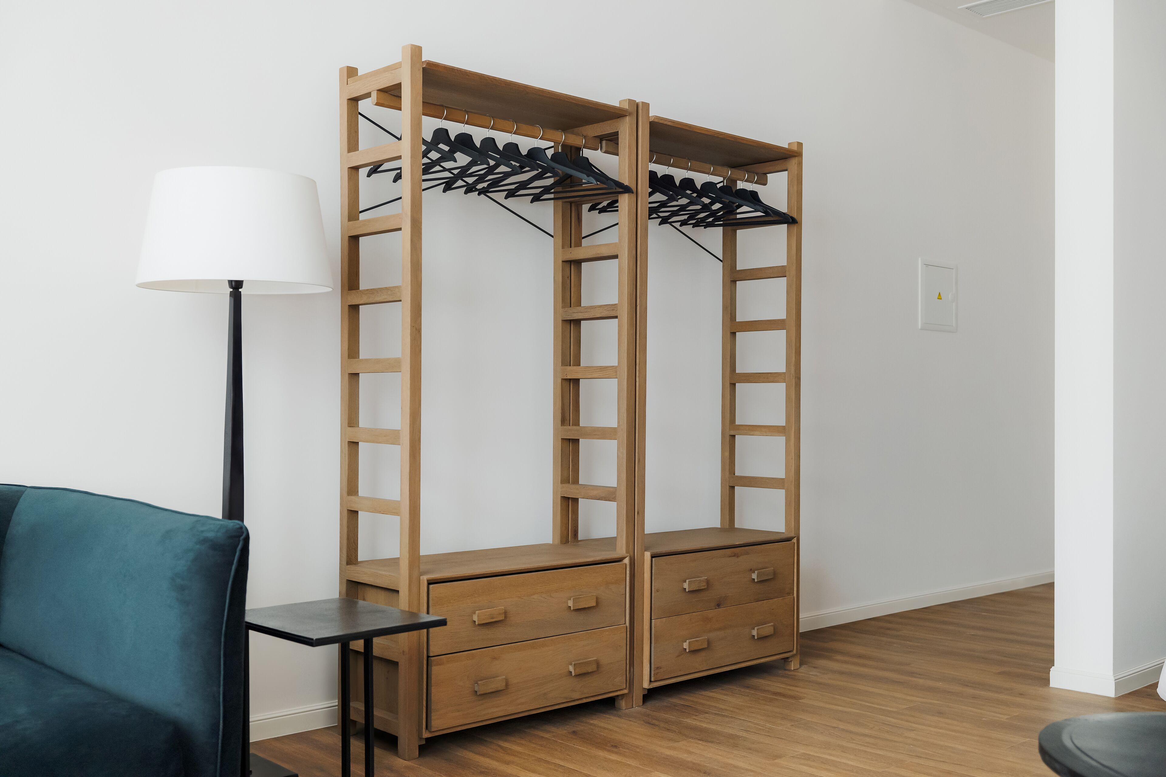 Een kamer met een houten garderobe, een klein tafeltje en een blauwgroene stoel.