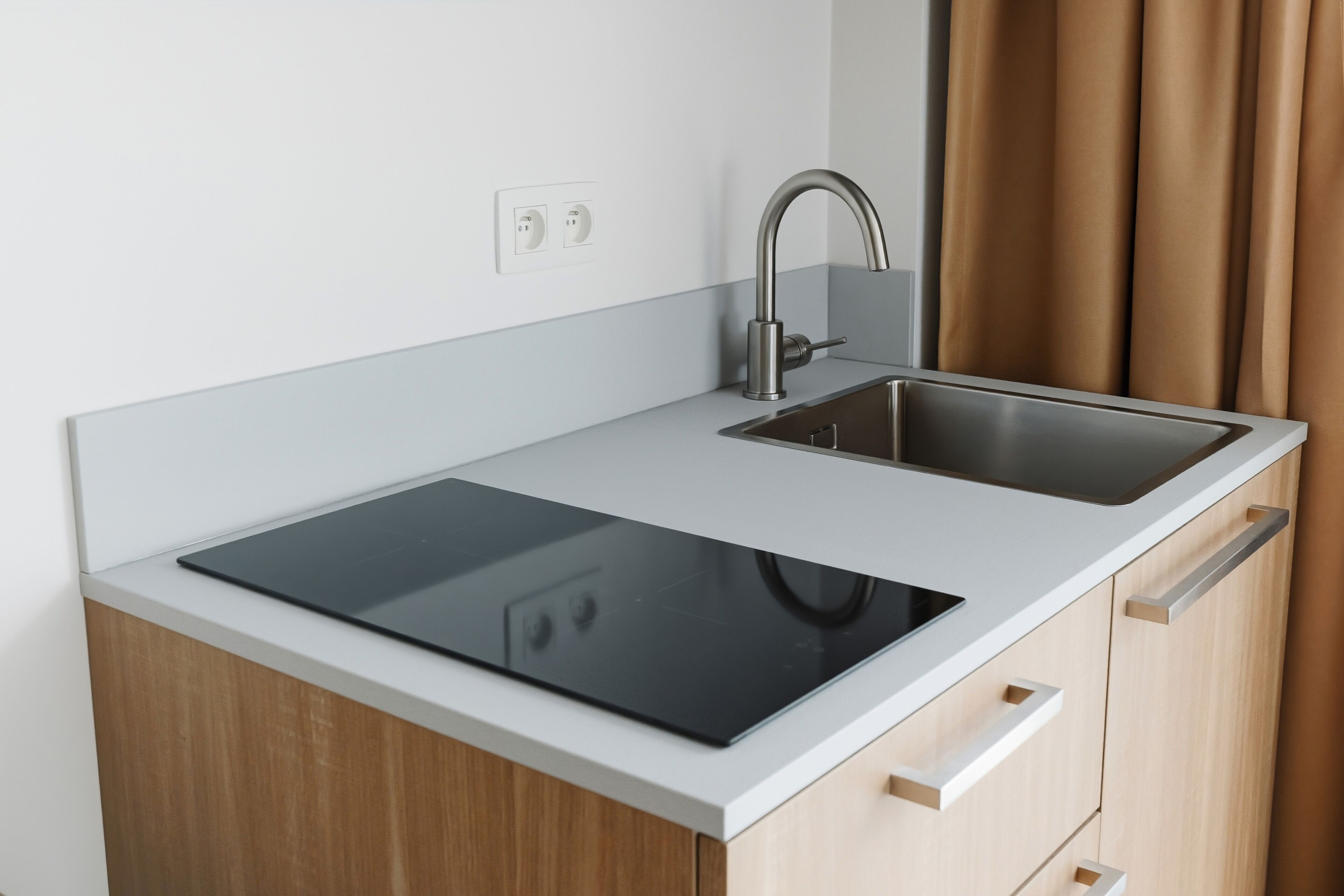 A modern kitchen with a black induction cooktop, stainless steel sink, and wooden cabinets.
