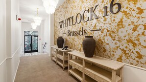 Een hal met een muur waarop 'WHITLOCK 16 Brussels' staat en twee grote vazen op een console tafel.