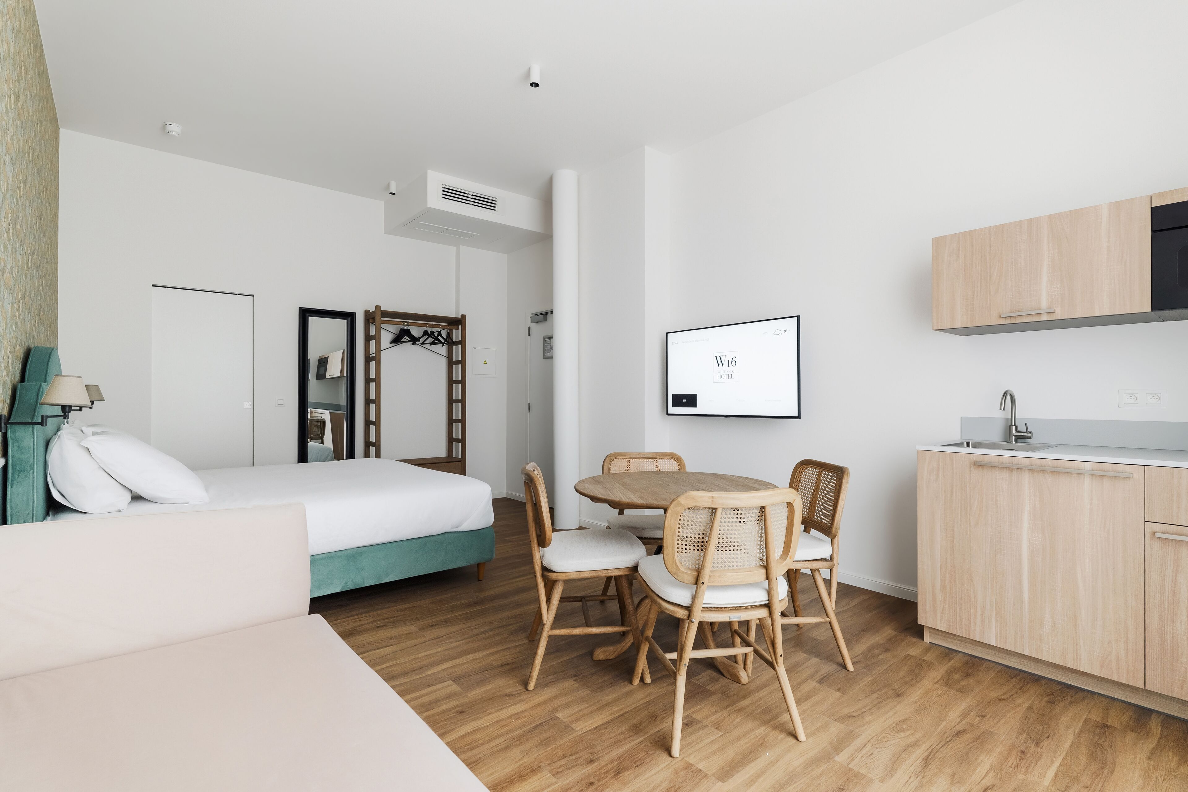 Une chambre d’hôtel moderne, équipée d’un lit, d’une table à manger avec des chaises, d’un coin cuisine et d’un tableau encadré au mur.