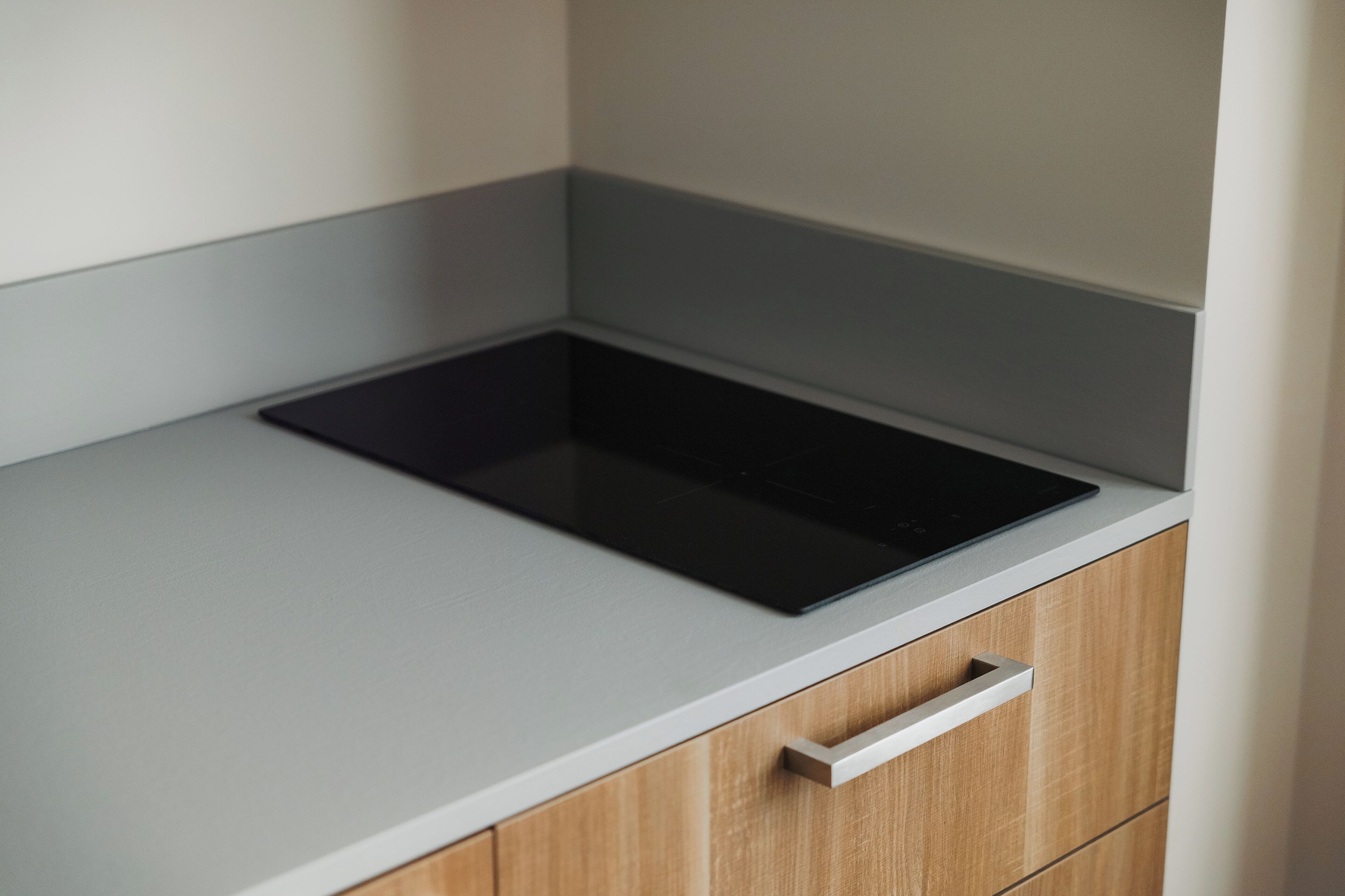 A kitchen with a black induction cooktop on a light grey countertop, a wooden cabinet below, and a white drawer.