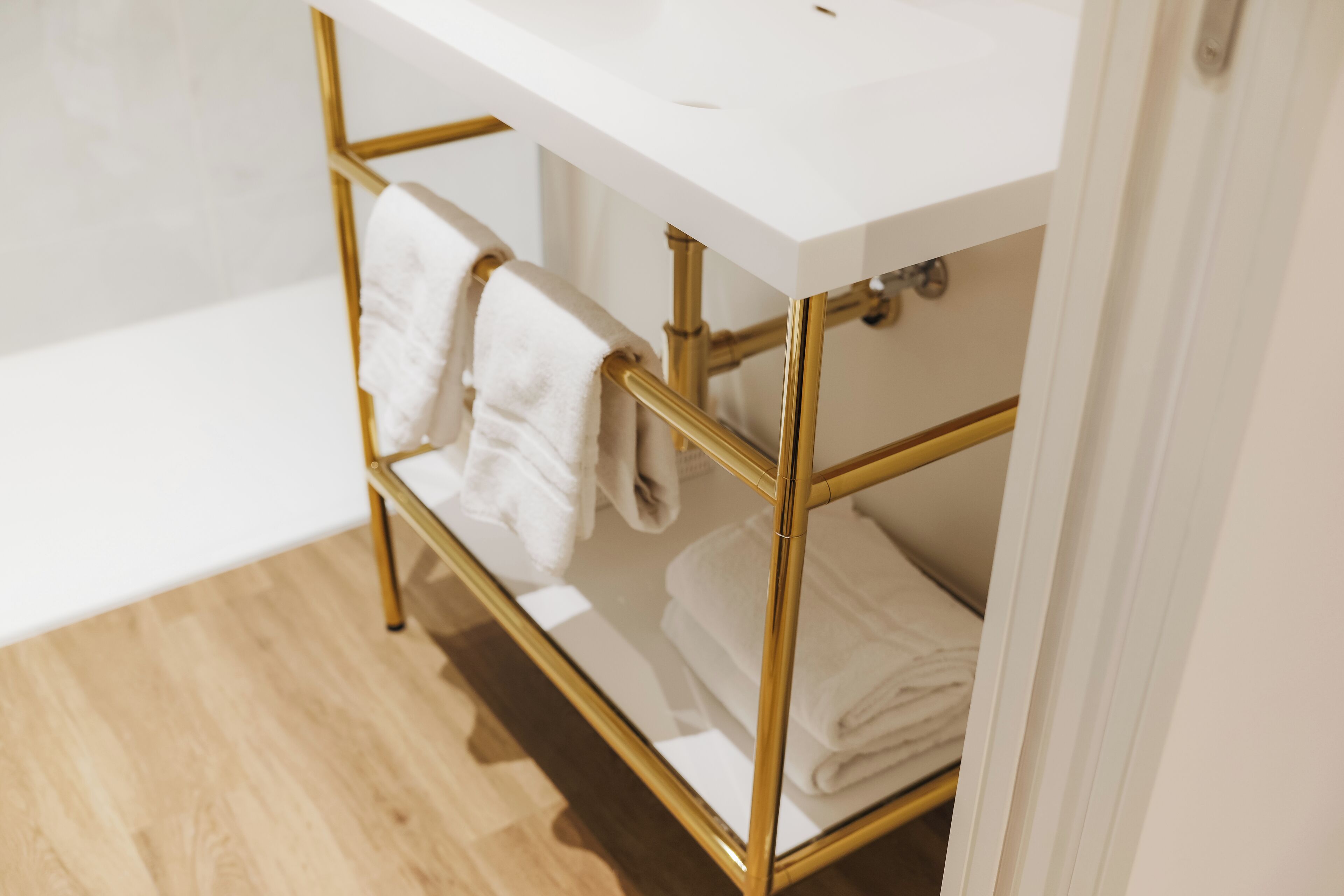 Een badkamer met een witte wastafel en gouden details, waaronder een handdoekrek en een wastafelmeubel.