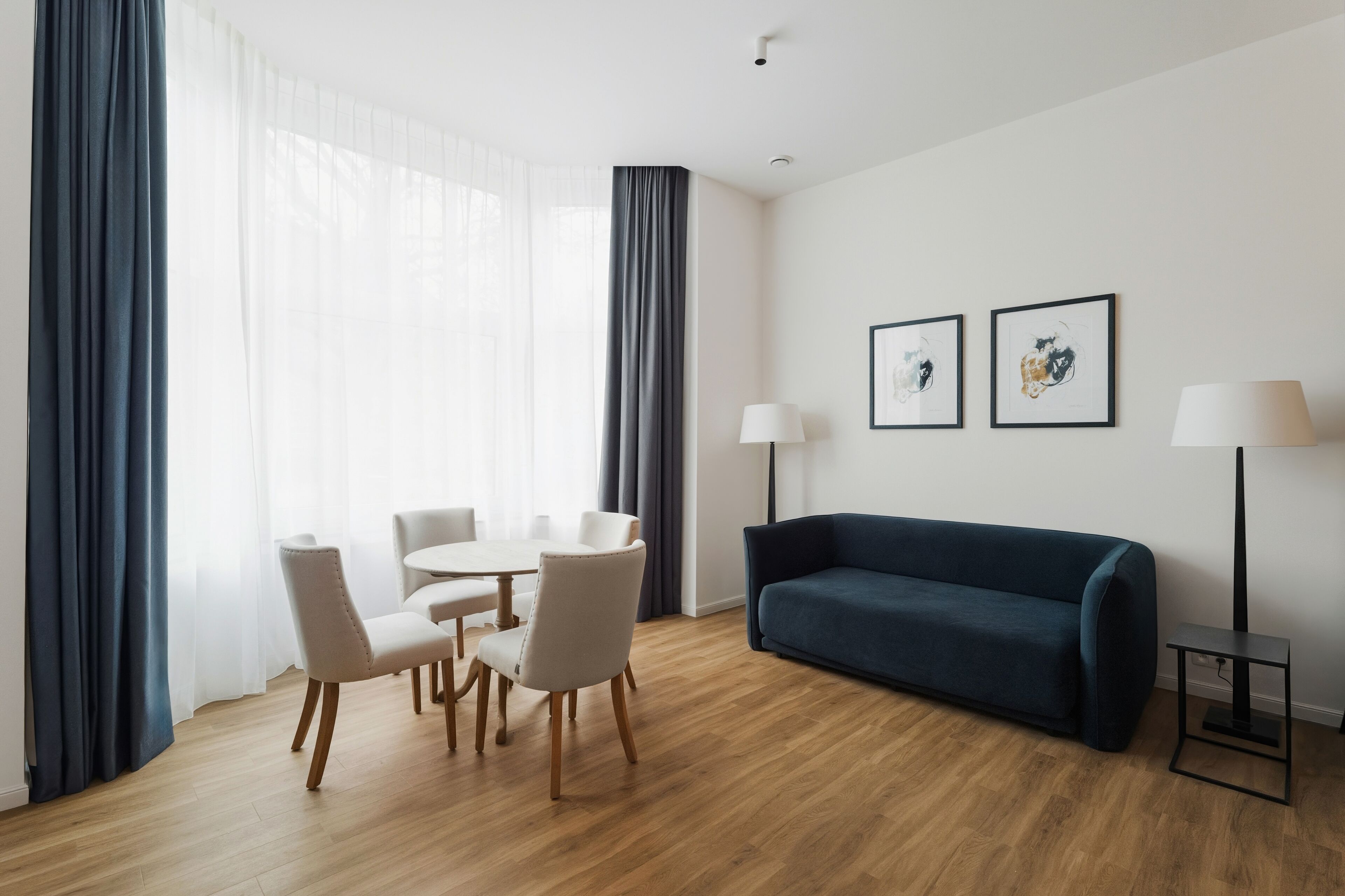 A modern living room with a dark blue sofa, a round dining table with chairs, and two wall-mounted lamps.