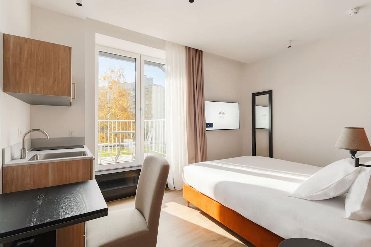 Een moderne hotelkamer met een bed, bureau en raam met uitzicht op gebouwen en bomen.