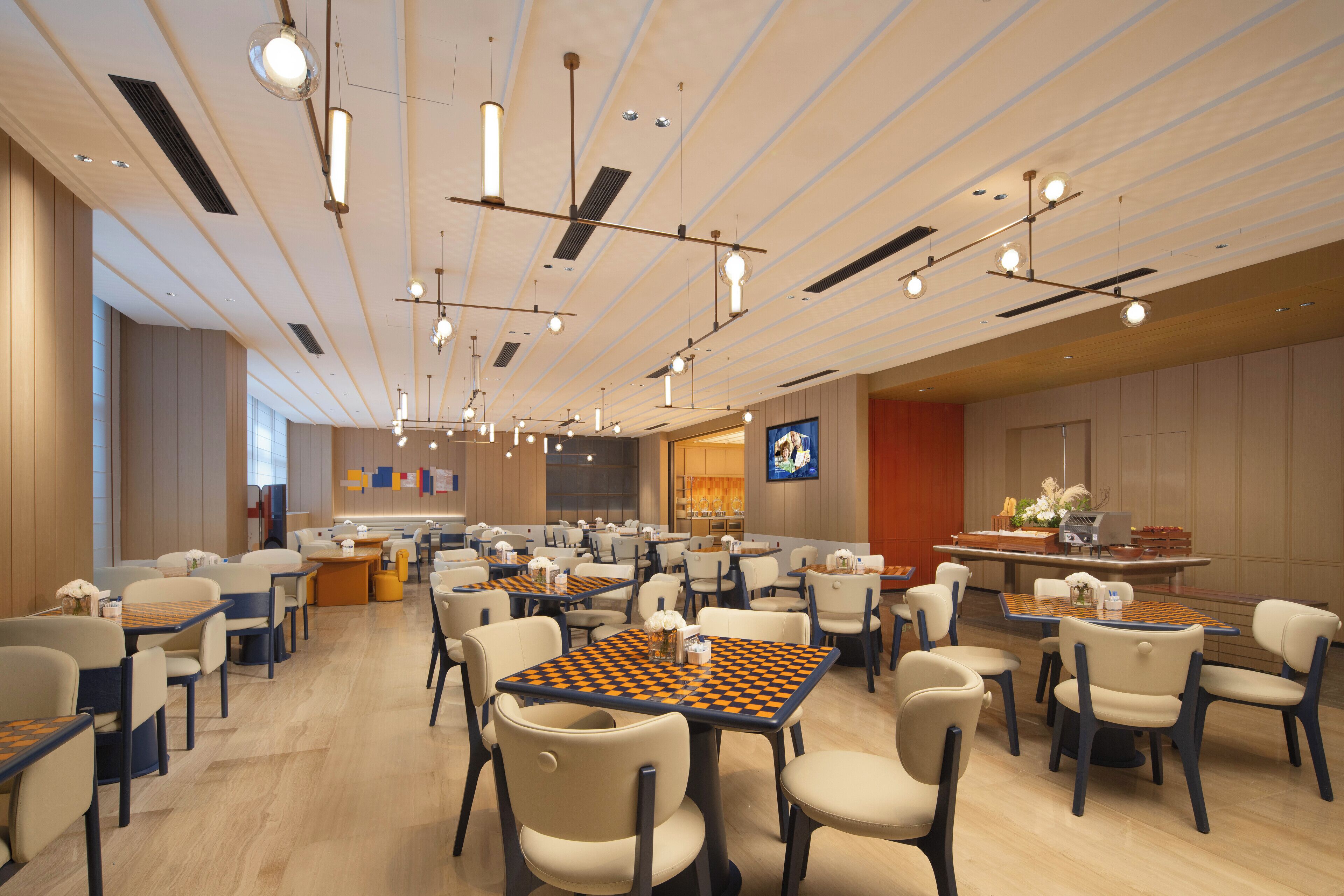 A spacious hotel lobby with multiple seating areas, including tables and chairs, and a large screen displaying content.