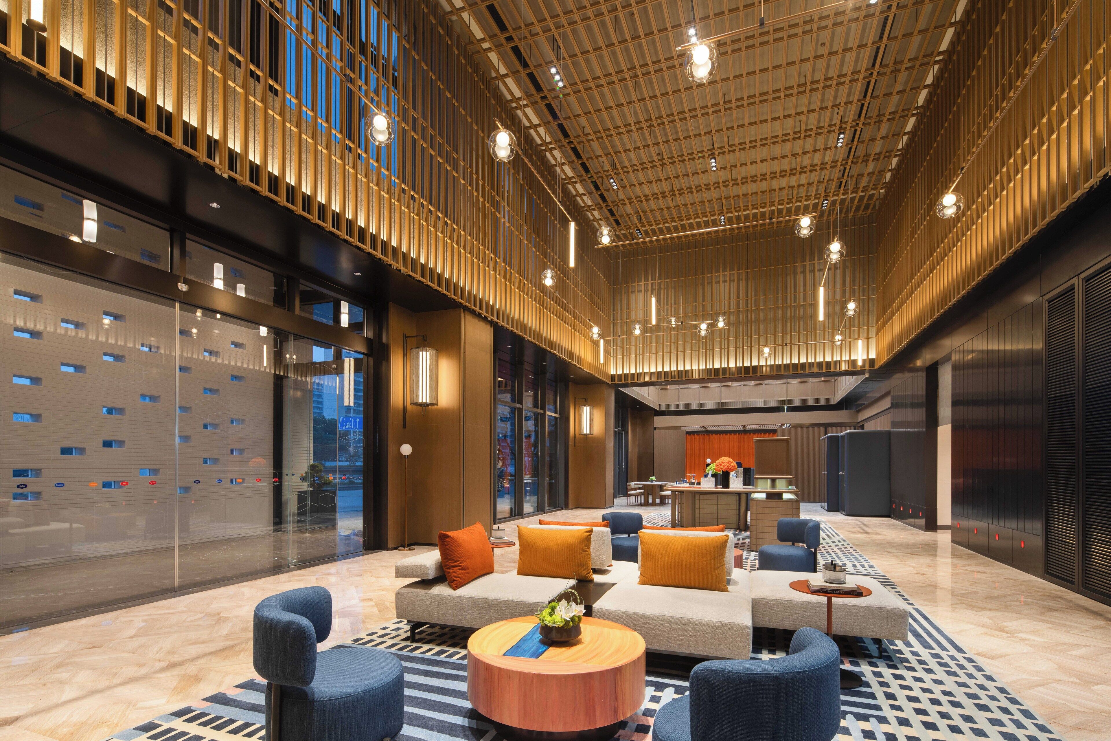 Un vestíbulo espacioso con diseño moderno, que presenta una zona de estar central con sofás y sillones, un suelo estampado y un techo con luminarias lineales.
