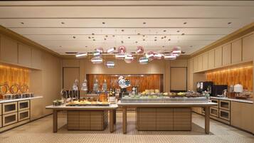 A modern hotel lobby with a buffet area, wooden paneling, and a large chandelier.