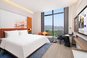 A modern hotel room with a large bed, a desk, and a view of a cityscape. - Hampton by Hilton Cixi Guanhaiwei (Ningbo)