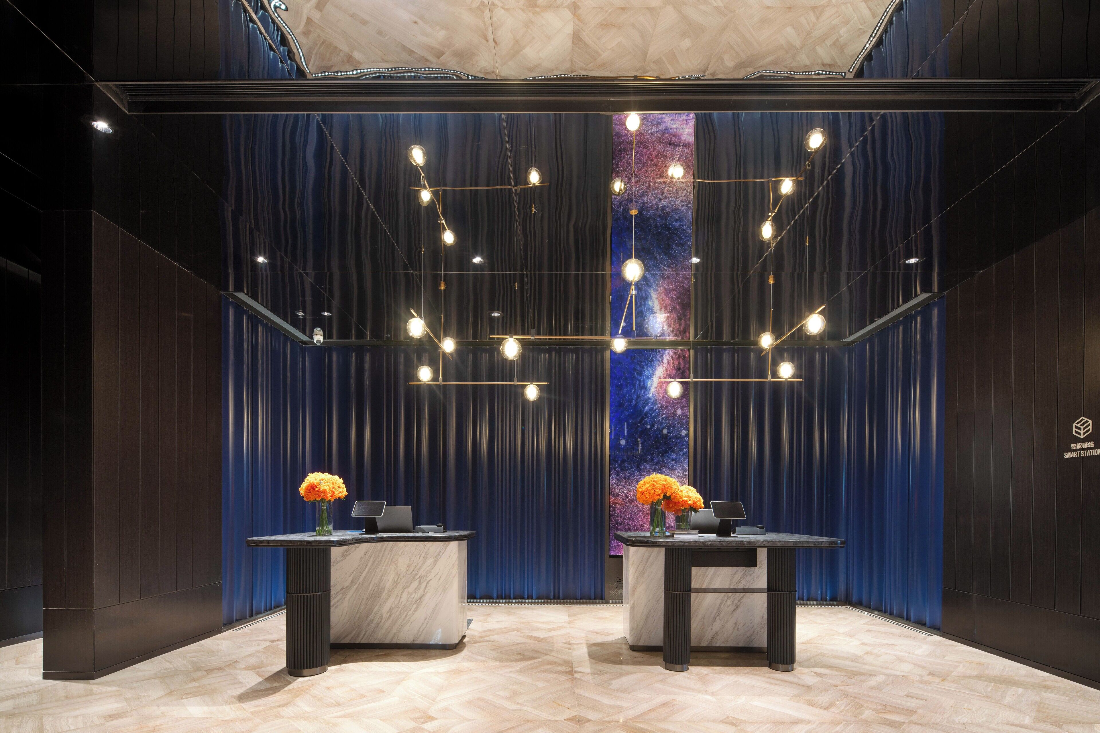 Een moderne lobby met twee receptiebalies, een grote muurschildering met een sterrenstelselthema en een plafond met hangende lampen.