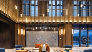 A modern hotel lobby with a seating area, a reception desk, and a large window with a view of the cityscape. - Hampton by Hilton Cixi Guanhaiwei (Ningbo)