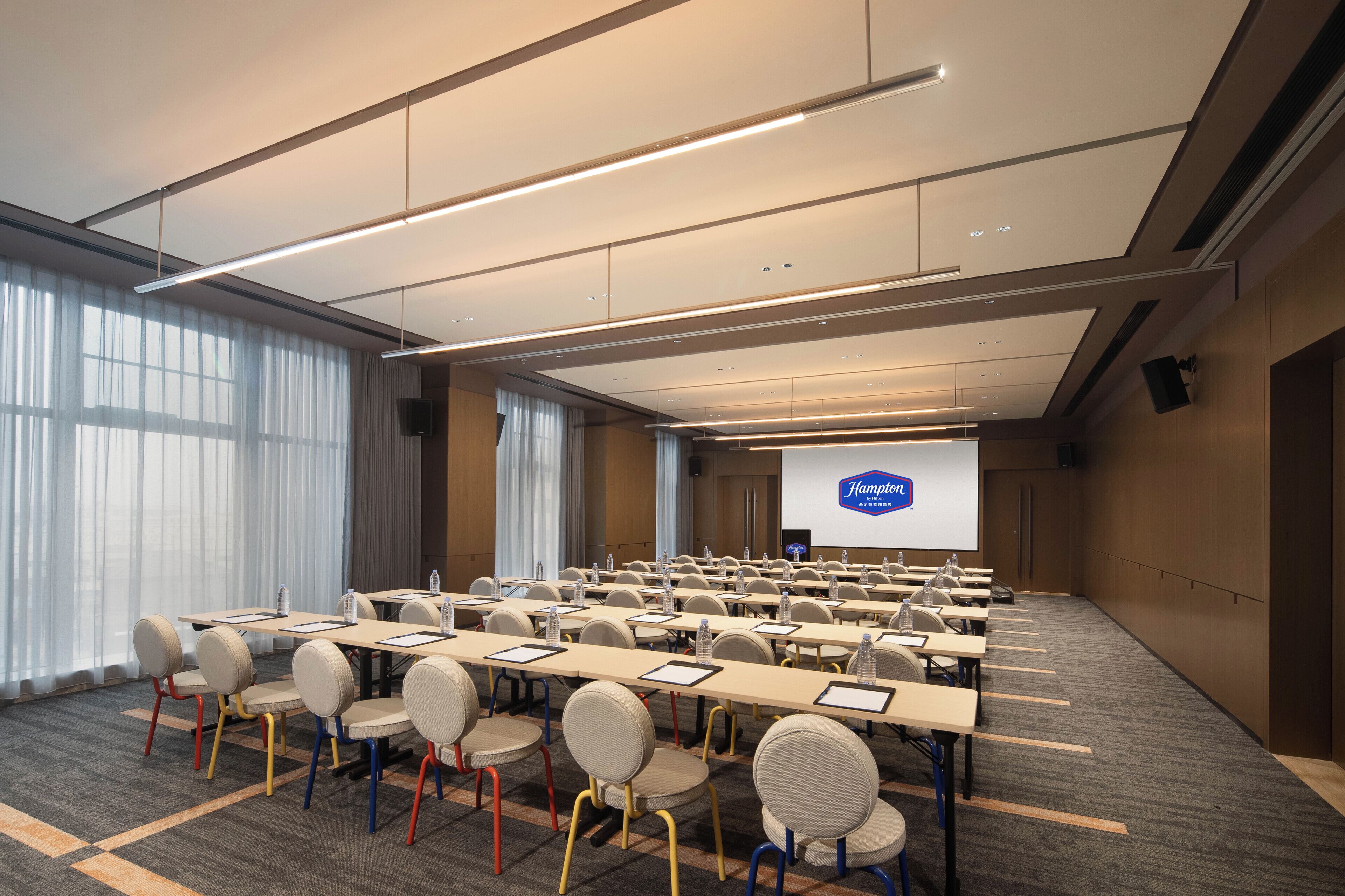 A conference room with rows of tables and chairs, a large screen, and a projector.