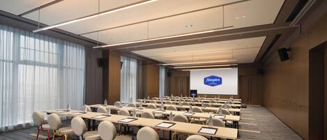 A conference room with rows of tables and chairs, a large screen, and a projector.