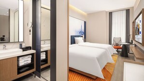 A hotel room with a large bed, a separate seating area, a bathroom with a mirror and sink, and a television. - Hampton by Hilton Cixi Guanhaiwei (Ningbo)