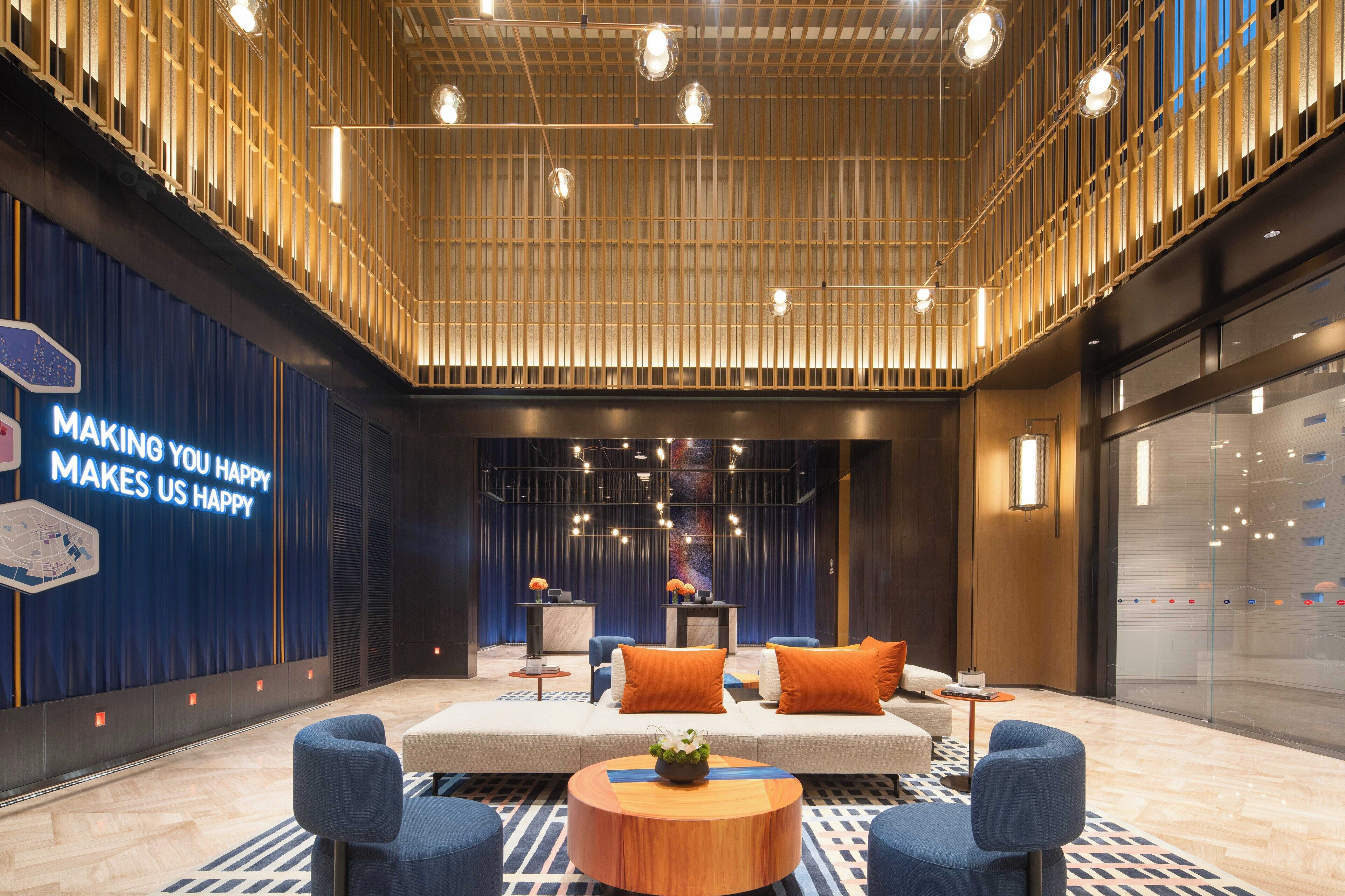 A modern lobby with a large sofa, blue chairs, a wooden coffee table, and a wall with a motivational quote.