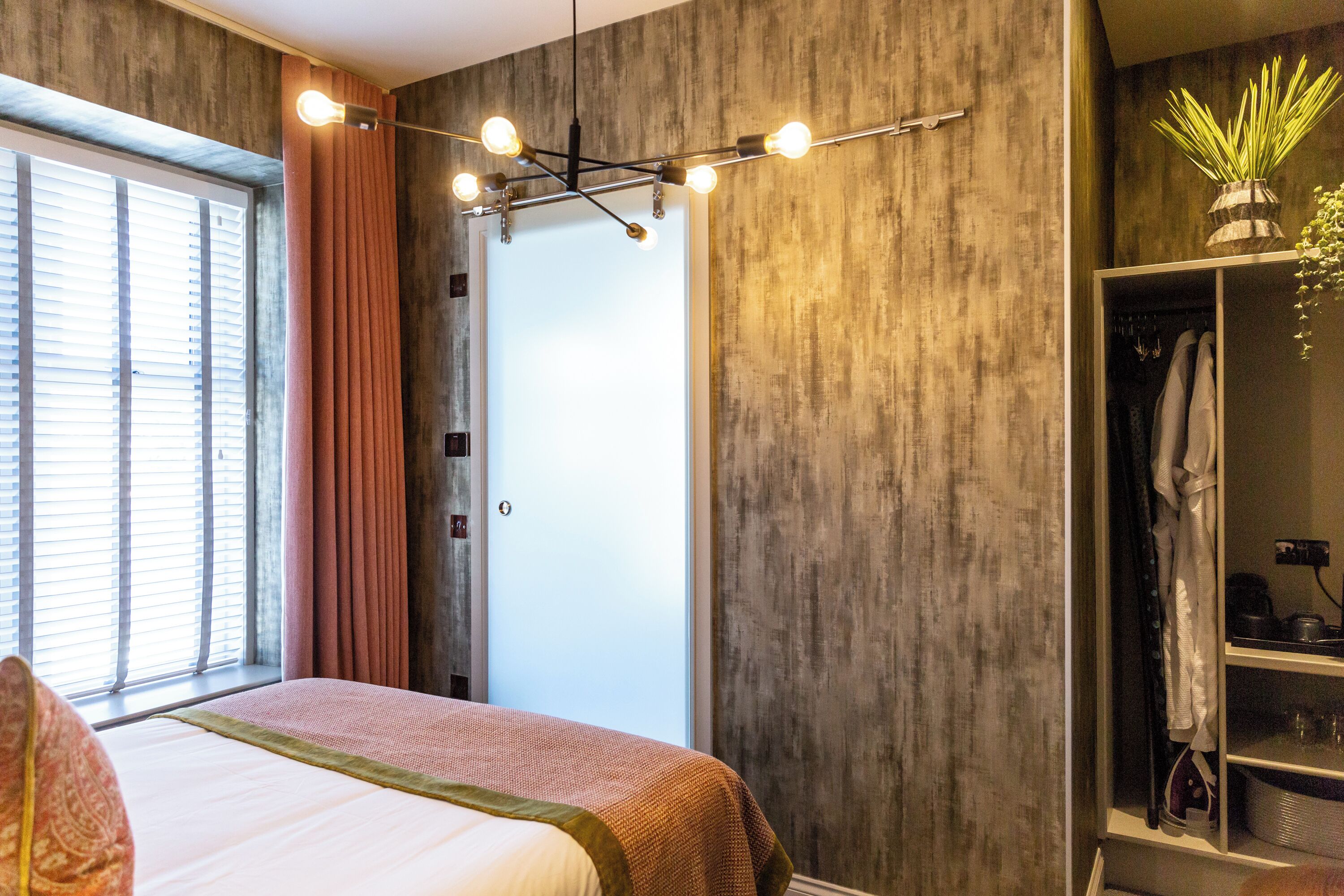 A modern bedroom with a large bed, a wardrobe, and a window with blinds.