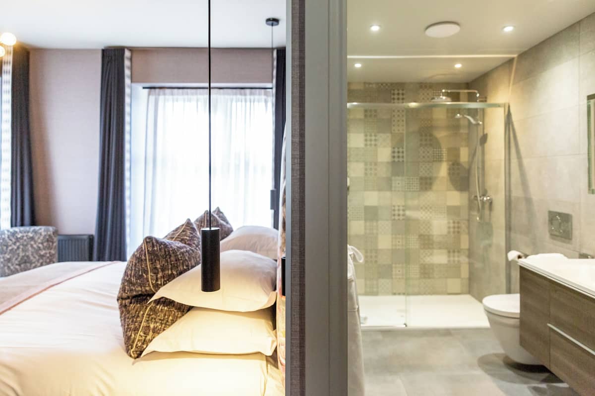 Una habitación de hotel moderna con una cama grande, cabina de ducha de vidrio y un baño independiente con inodoro y lavamanos.