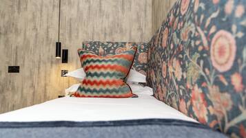 A bed with a patterned pillow, a floral upholstered headboard, and a wall-mounted light fixture.