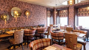 Een restaurantinterieur met behang met patroon, ronde tafels en geruite stoelen.