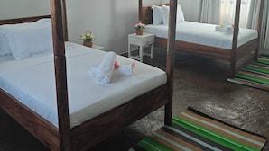 Een kamer met twee houten hemelbedden, witte beddengoed, een klein nachtkastje met een lamp, en een gestreept vloerkleed.