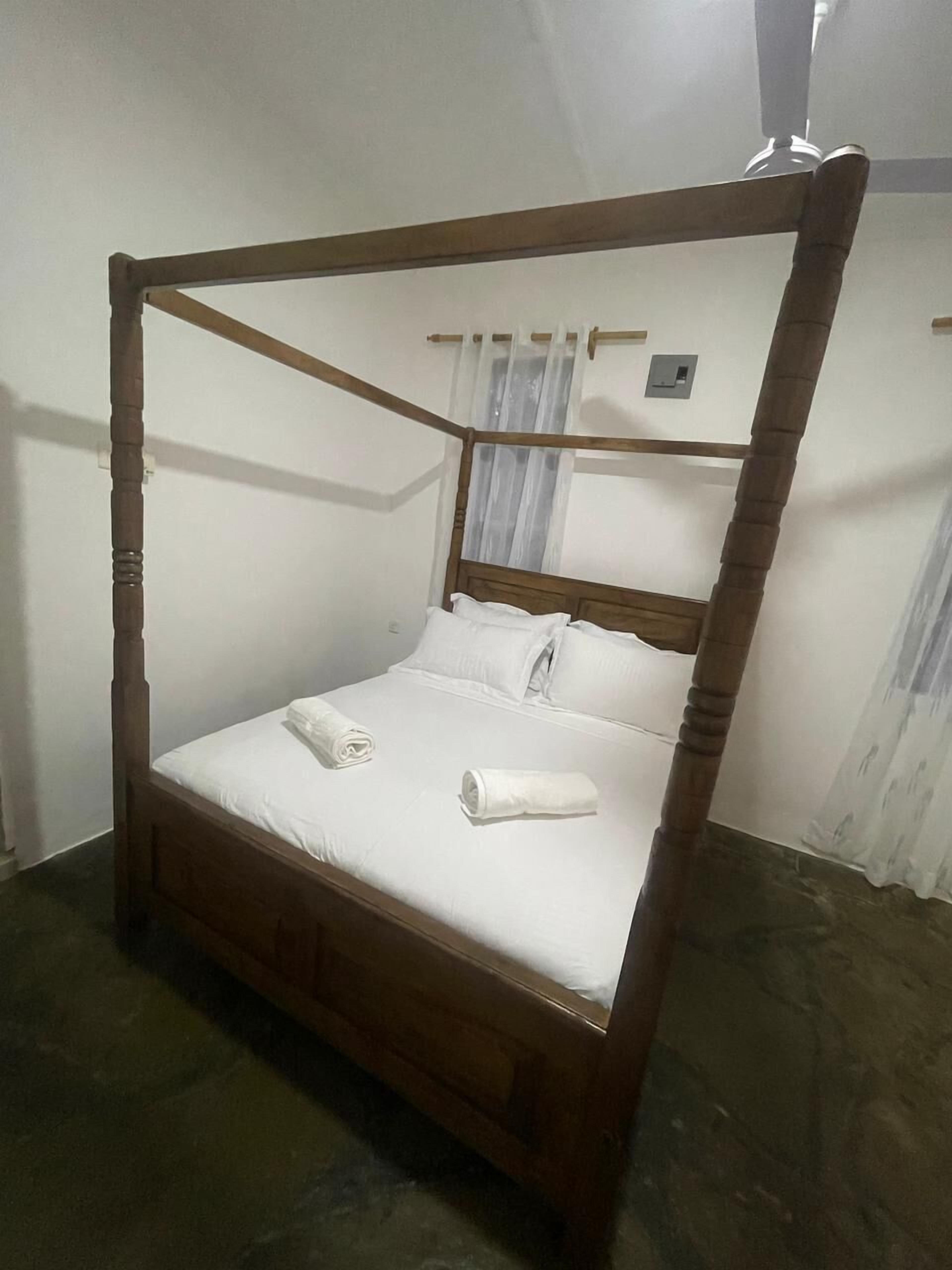 Un lit à baldaquin avec du linge de lit blanc et deux serviettes enroulées.