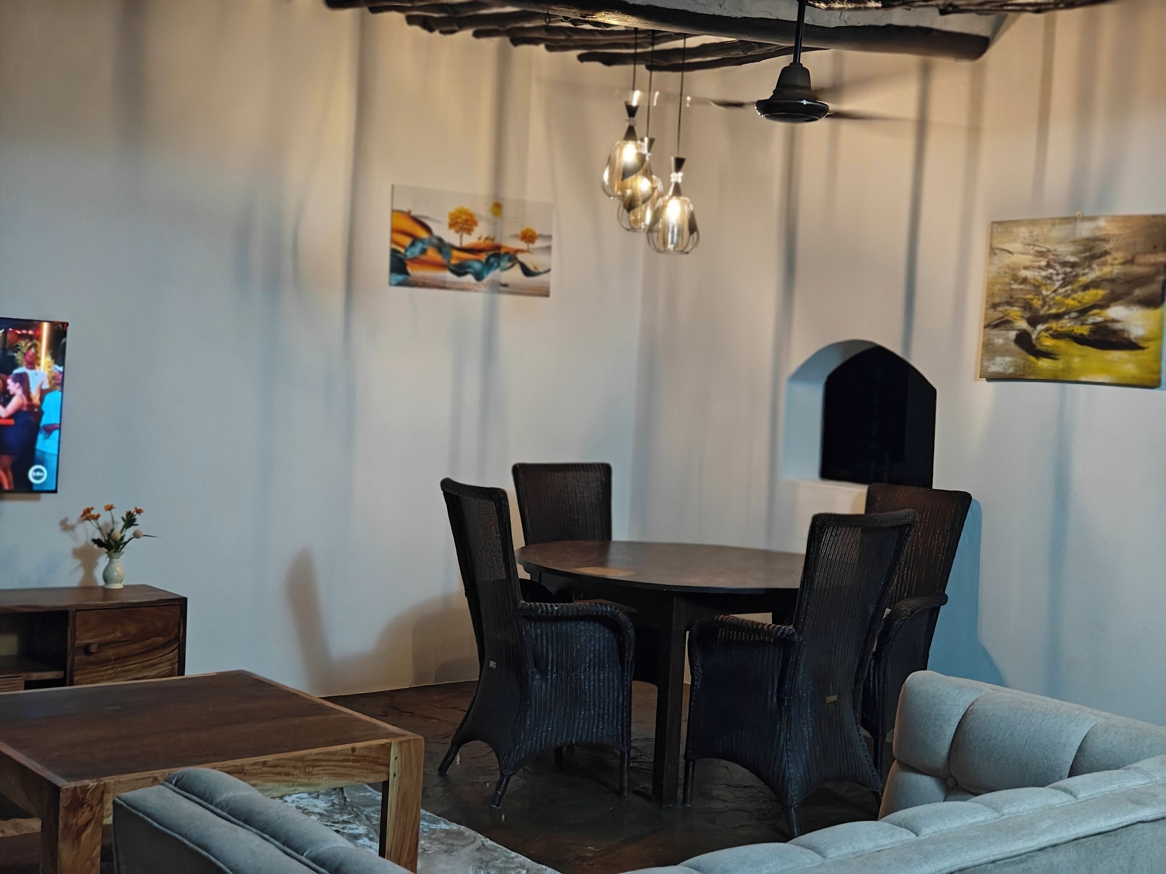 A dining area with a round table, four chairs, a ceiling fan, and hanging pendant lights.