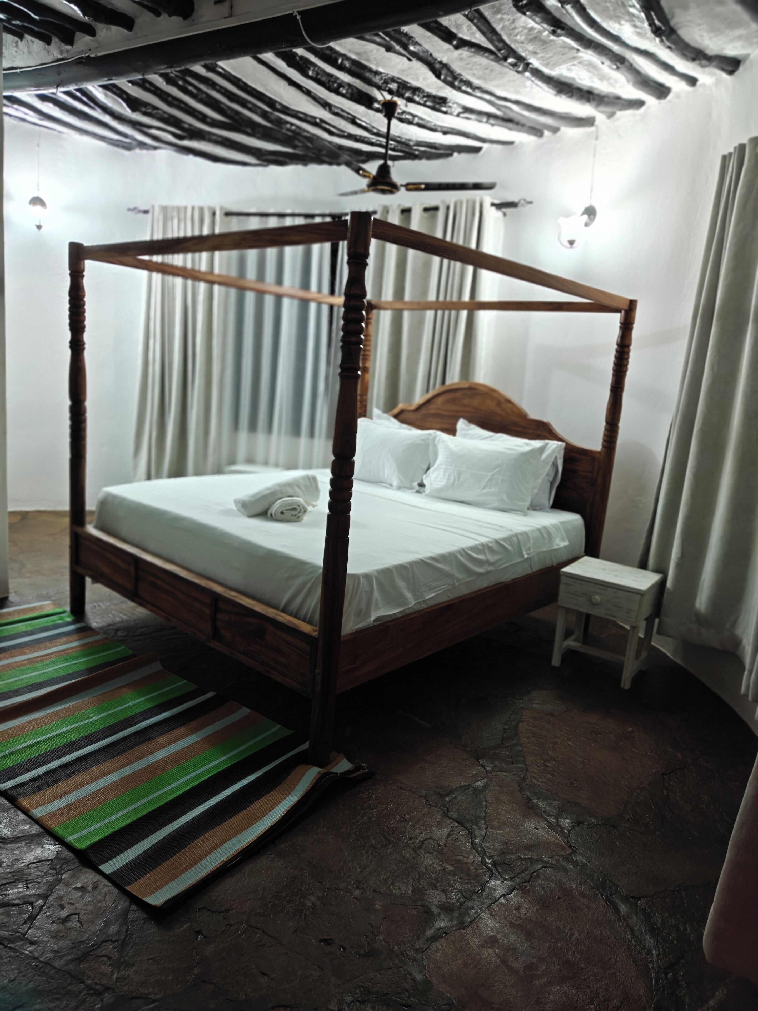 Un lit à baldaquin avec du linge de lit blanc, une tête de lit en bois et une petite table de chevet.