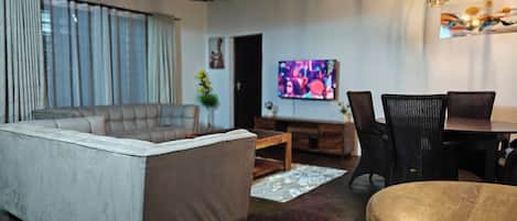 A modern living room with a sofa, dining table, and chairs, a television, and a ceiling with exposed beams.