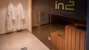 Un baño de hotel con separador de vidrio, dos albornoces blancos colgados en ganchos y un banco de madera.