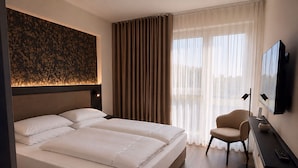 Habitación de hotel con una cama grande, un escritorio, una silla, un televisor de pantalla plana y una ventana con cortinas.