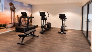 Un gimnasio con cintas de correr, elíptica y bicicleta estática, que presenta un mural con vista a la ciudad en la pared.