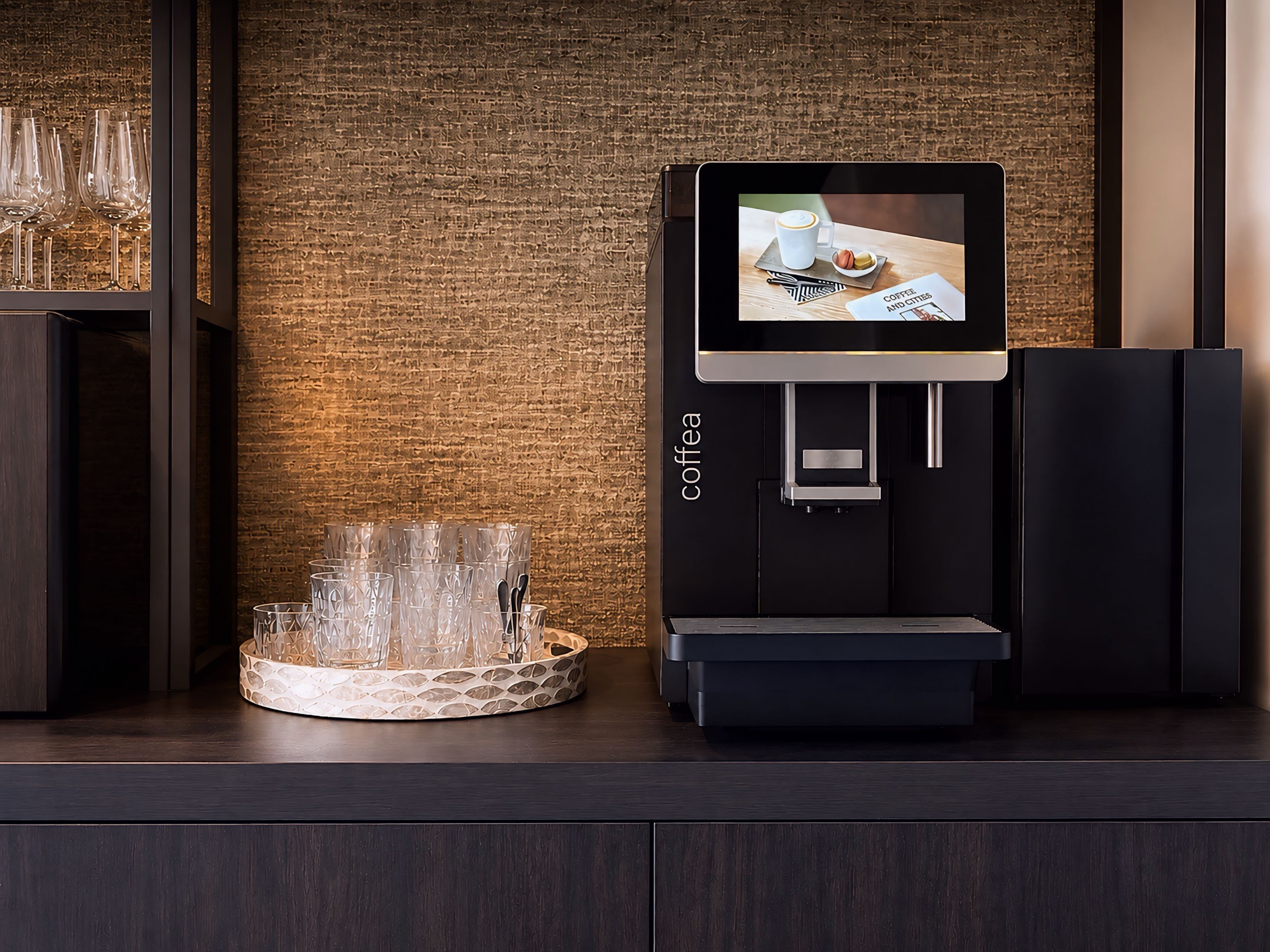 A coffee machine with a digital display, a glass container with glasses, and a brick wall background.