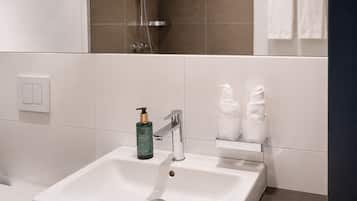 A modern bathroom with a white sink, a handheld showerhead, and a towel rack with two white towels.
