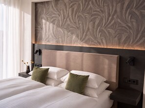 A hotel room with a large bed, two bedside tables, and a wall with a feather-like pattern. - In2 The Hotel (Xanten)