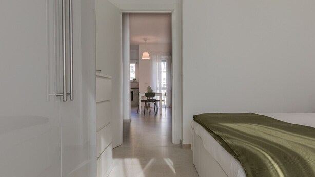 A modern bedroom with a bed, a green throw, and a hallway leading to a dining area. - Tripoli White Home by Wonderful Italy (Turin)