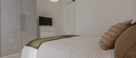 A bedroom with a bed, a television on a stand, a wardrobe, and a hanging light fixture.