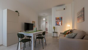 A modern living room with a sofa, a dining table with chairs, a television, and artwork on the walls. - Tripoli White Home by Wonderful Italy (Turin)