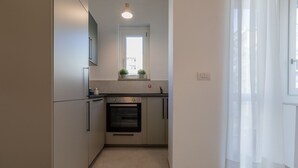 A compact kitchen with a built-in oven, a window above the sink, and a door leading to the living area. - Tripoli White Home by Wonderful Italy (Turin)