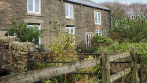 A stone house with multiple windows and a wooden fence in front. - The Farmhouse (High Peak)