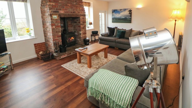 A living room with a brick fireplace, a sofa, a coffee table, and a television. - The Farmhouse (High Peak)