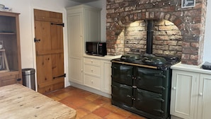 A kitchen with a brick wall, a stove, a microwave, and wooden cabinets. - The Farmhouse (High Peak)