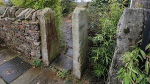 A stone wall with a metal gate, a stone pathway, and lush greenery. - The Farmhouse (High Peak)
