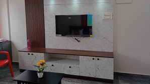 A modern room with a flat-screen TV mounted on a marble-patterned wall, a wooden cabinet below, and a small table with a vase of flowers.