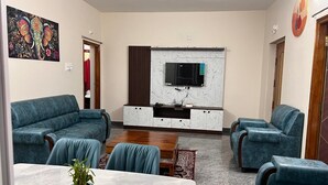 A living room with a TV, blue sofas, a wooden coffee table, and a potted plant.