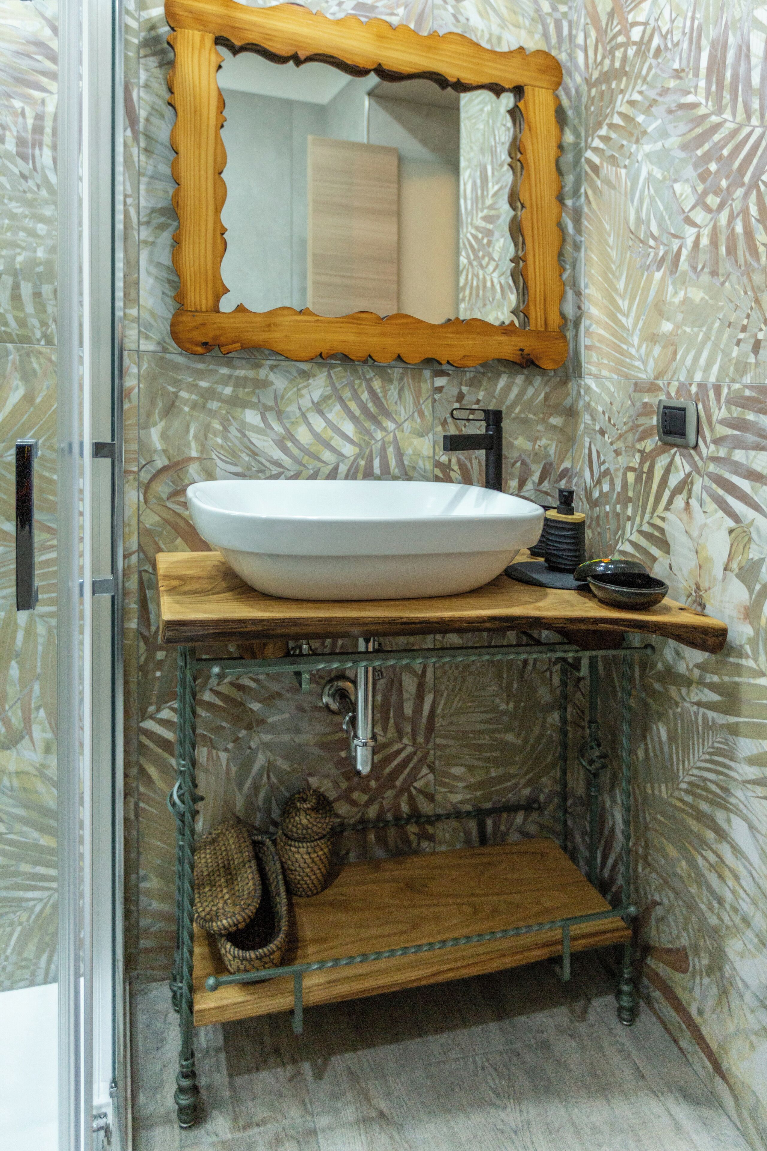 A bathroom with a large vessel sink, a wooden vanity, a mirror, and a shower area.