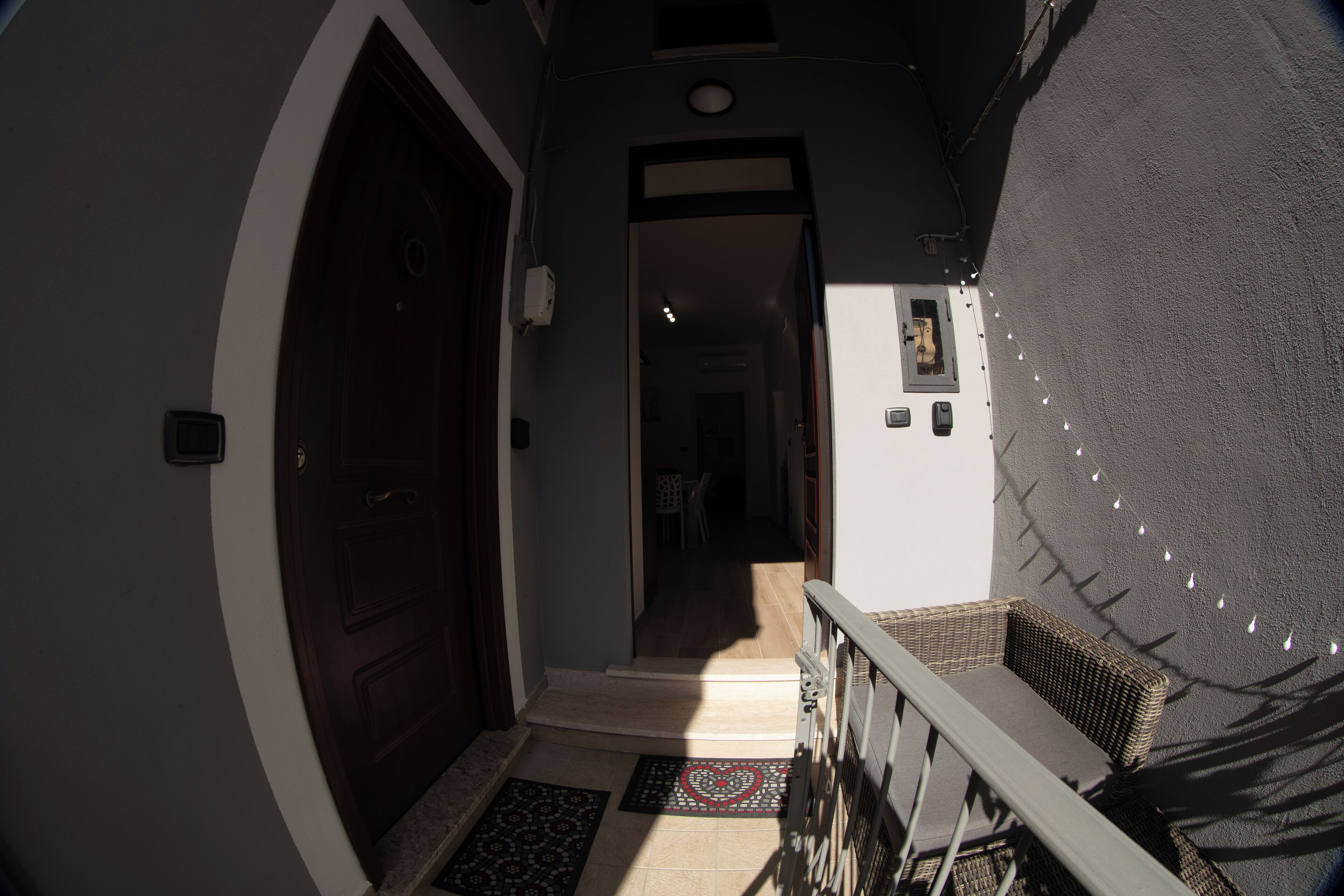 A hallway with a wooden door, a small staircase, and a wicker chair by the railing.