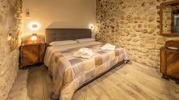 A bedroom with a stone wall, a bed with a checkered bedspread, a bedside lamp, and a wooden nightstand.