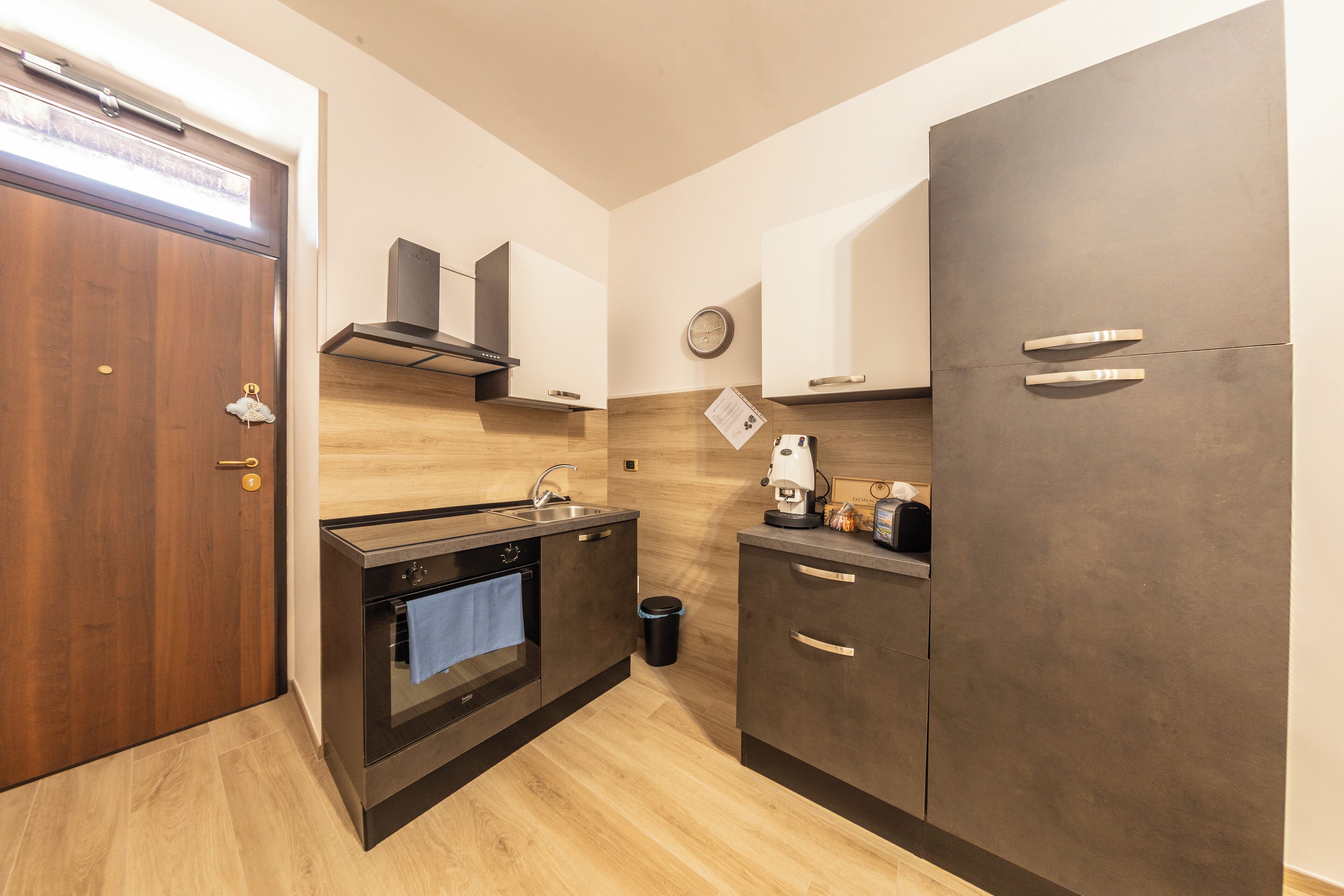 A compact kitchen with a wooden door, a built-in oven, a sink, and a coffee machine.